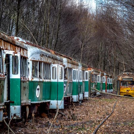 Abandoned trolley graveyard with Boston MBTA, MTA, Pittsburgh area transit car and track surrounded by trees.
