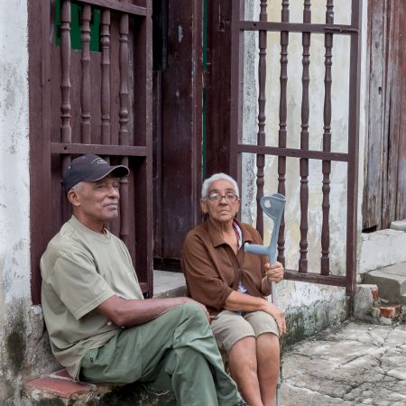 Cuban couple sitting on curb outside of home.