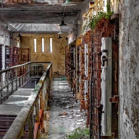 Abandoned Pennsylvania Eastern State Penitentiary cellblock with screened central opening to lower floor, moss and rust.