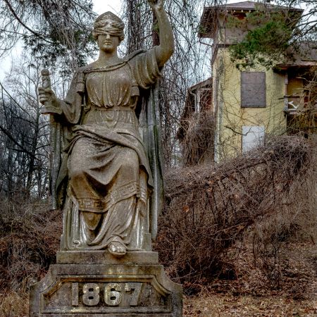 National Park Seminary, Forest Glen, Maryland abandoned 1867 statue of Justice with vines and derelict Italian villa style dormitory in background.