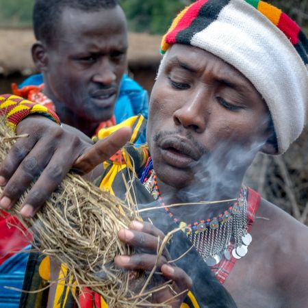 Maasai warrior in traditional dress and making fire.