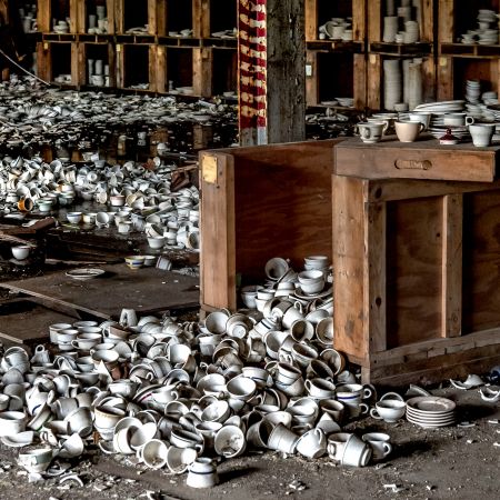 Abandoned china factory with shelves of cups and saucers, as well as many on floor.