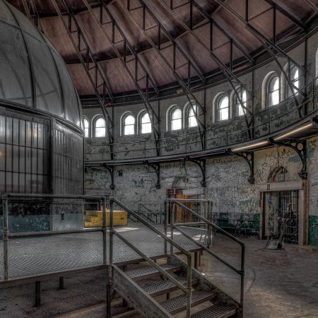 Central location of cellblocks in abandoned prisons with dome like structure at center point, and a circle of arched windows below wood ceiling.