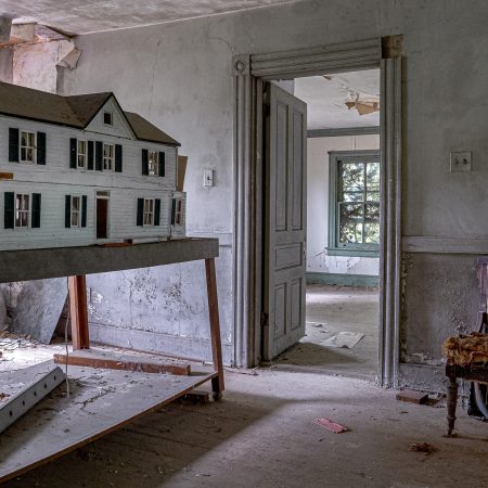 The irony of an abandoned house inside a forlorn house with a dollhouse and tattered upholstered chair as the only remaining occupants.