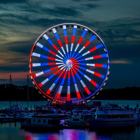 National Harbor Ferris wheel at sunset with boats in marina.