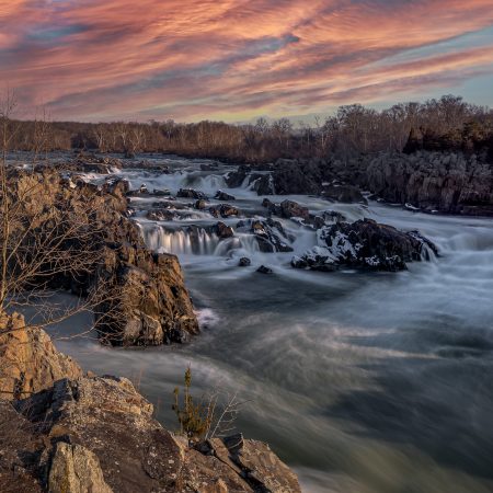 Winter sunrise at Virginia side of Great Falls National Park with white water rapids and orange clouds.