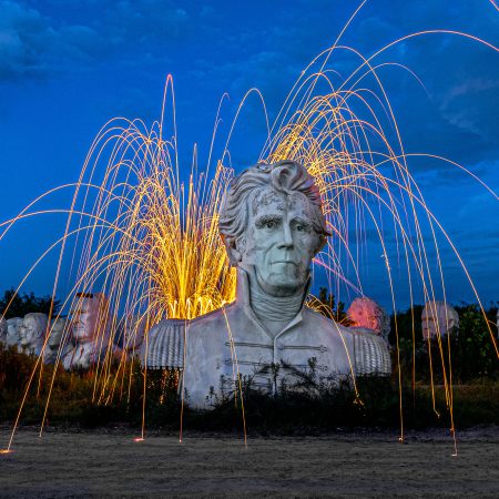 Steel Wool Spinning at blue hour behind 20 ft tall concrete presidential heads with George Washington and Andrew Jackson and Abraham Lincoln in forefront.