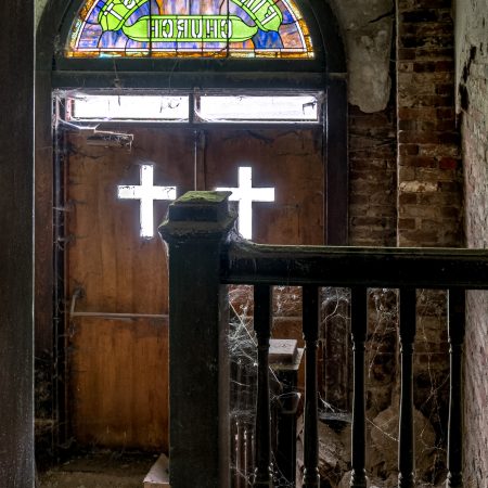 Abandoned church entrance with stained glass, exposed brick, peeling paint and spider webs.