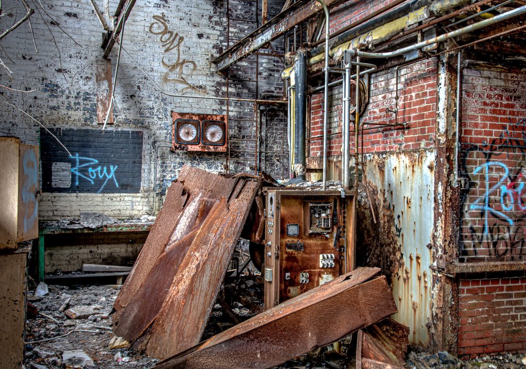 The abandoned power plant of an abandoned hospital with rusty control panels and graffiti on the brick walls.