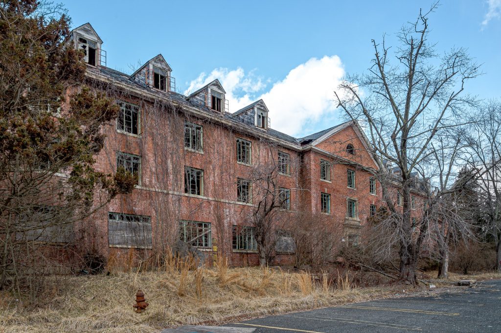 Derelict Henryton Tuberculosis Sanitarium with broken windows, red brick and tall weeds.