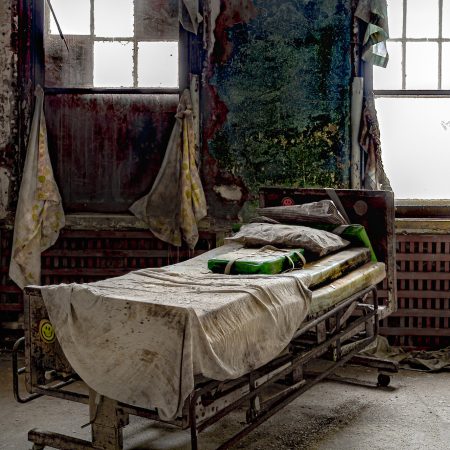 Abandoned Pennsylvania Pennhurst Asylum hospital ward with hospital bed and linens.